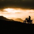 "Motorcyclist riding gloves and gear silhouetted against mountain sunset, India"