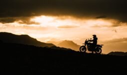 "Motorcyclist riding gloves and gear silhouetted against mountain sunset, India"