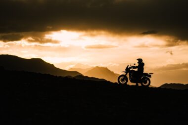 "Motorcyclist riding gloves and gear silhouetted against mountain sunset, India"