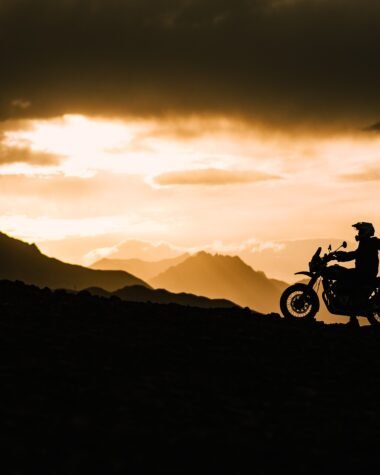 "Motorcyclist riding gloves and gear silhouetted against mountain sunset, India"