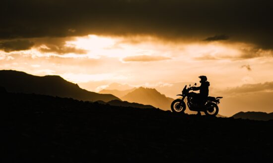 "Motorcyclist riding gloves and gear silhouetted against mountain sunset, India"