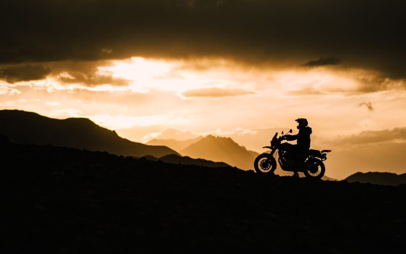 "Motorcyclist riding gloves and gear silhouetted against mountain sunset, India"